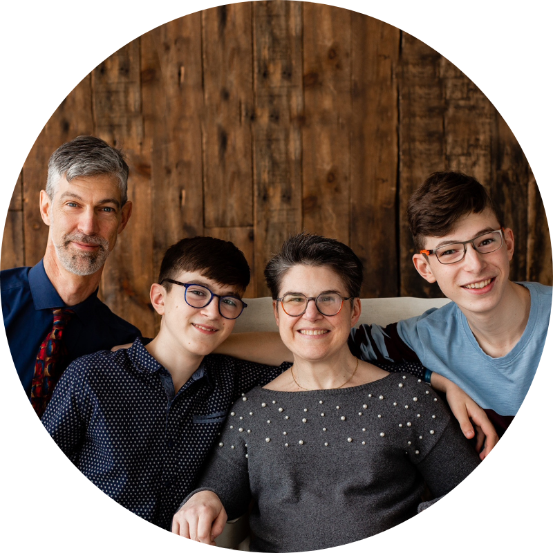 Famille de quatre personnes assise devant un mur en bois, posant avec les bras autour les uns des autres.