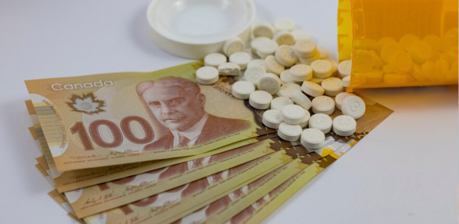 Canadian $100 bills spread on a surface beside a prescription pill bottle with white tablets spilled out.