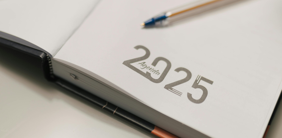 Close-up of an open planner labeled ‘2025 Agenda’ on a desk, with a pen resting on the page.